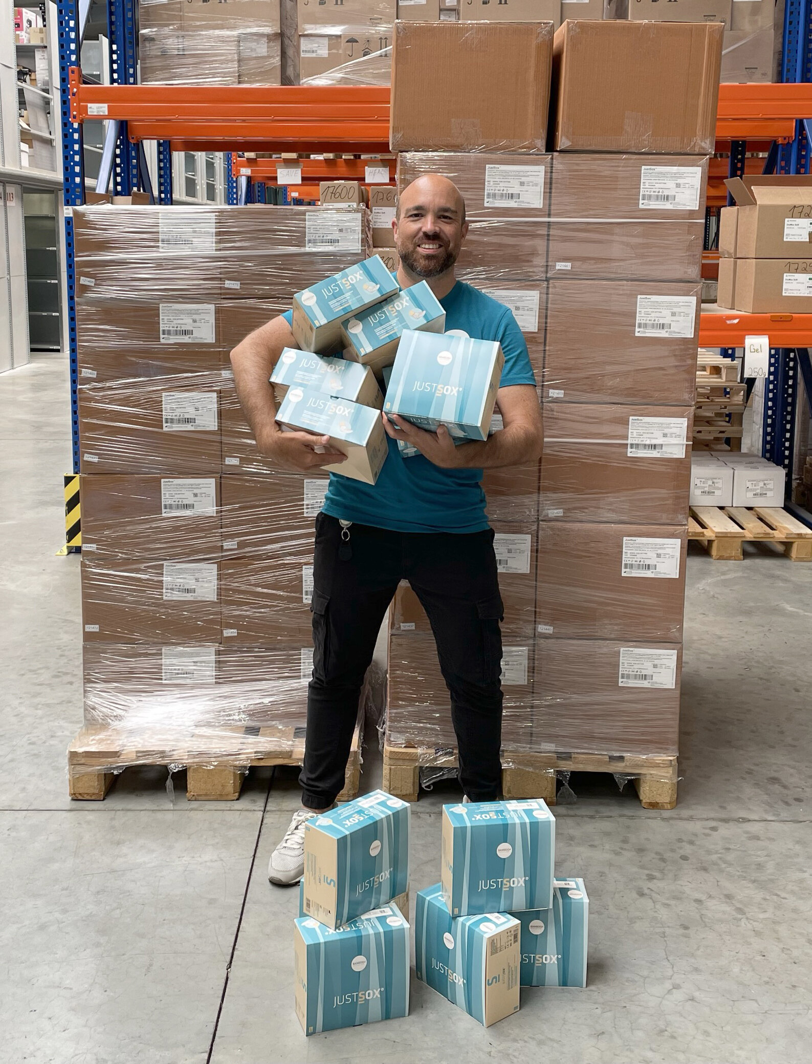 Felix Zimmermann steht mit JustSox® Verpackungen im Arm vor einer Palette JustSox®, vor ihm auf dem Boden weitere Verpackungen gestapelt als Gruppe. | © Bamboo Health Care GmbH